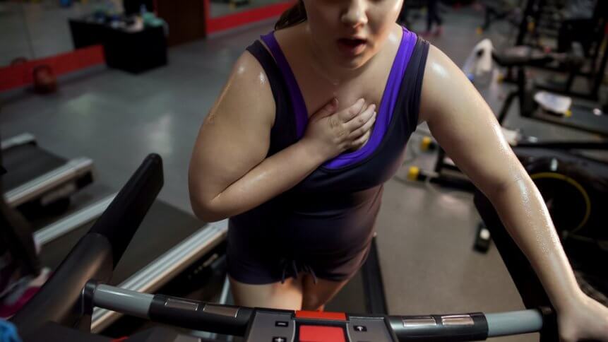 Woman exercising on treadmill wrong way, breathing heavily, having chest pain