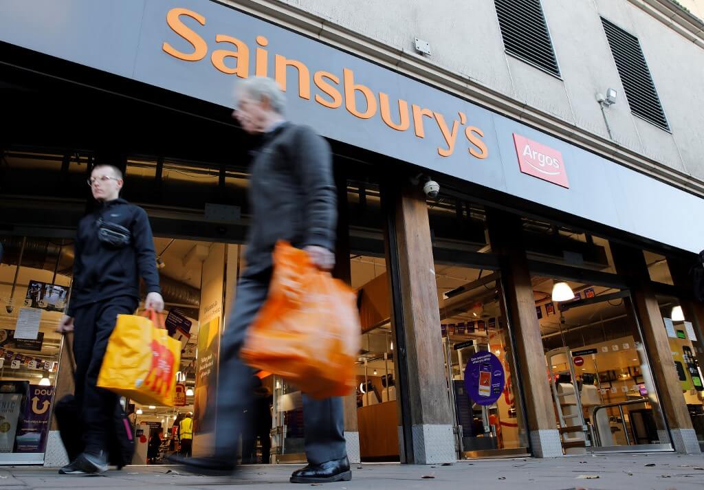 Pedestrians walk past a sign above the entrance to a Sainsbury's supermarket store in London.