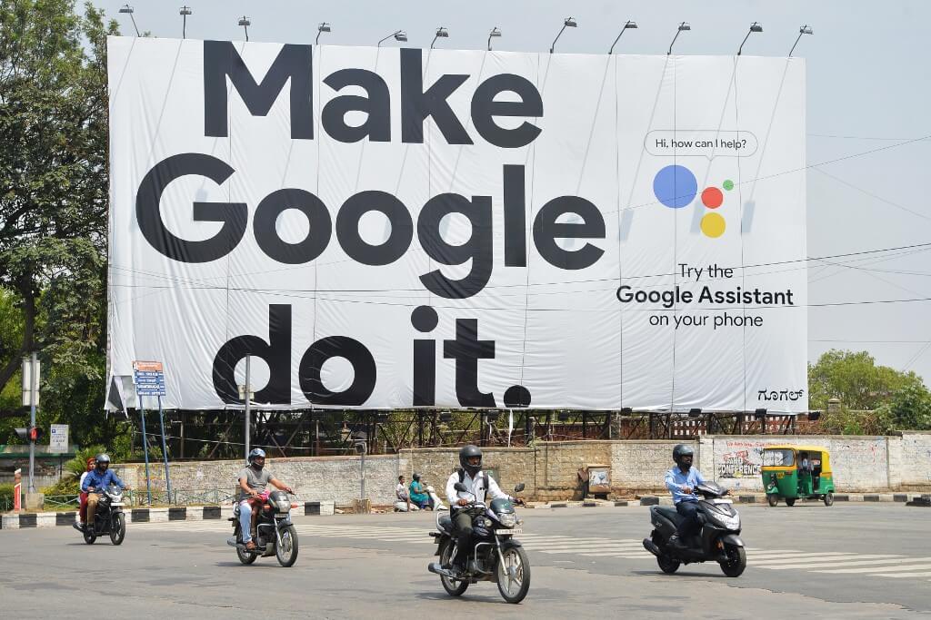Indian commuters ride past an advertisement poster of Google in Bangalore